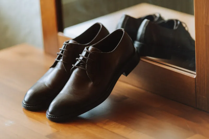 brown men's leather shoes on the wooden floor near the mirror