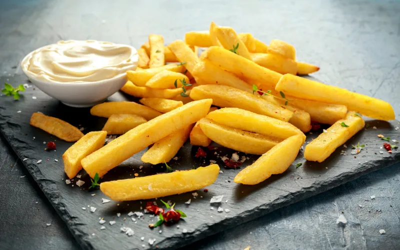 homemade baked potato fries with mayonnaise, salt, pepper on black stone board