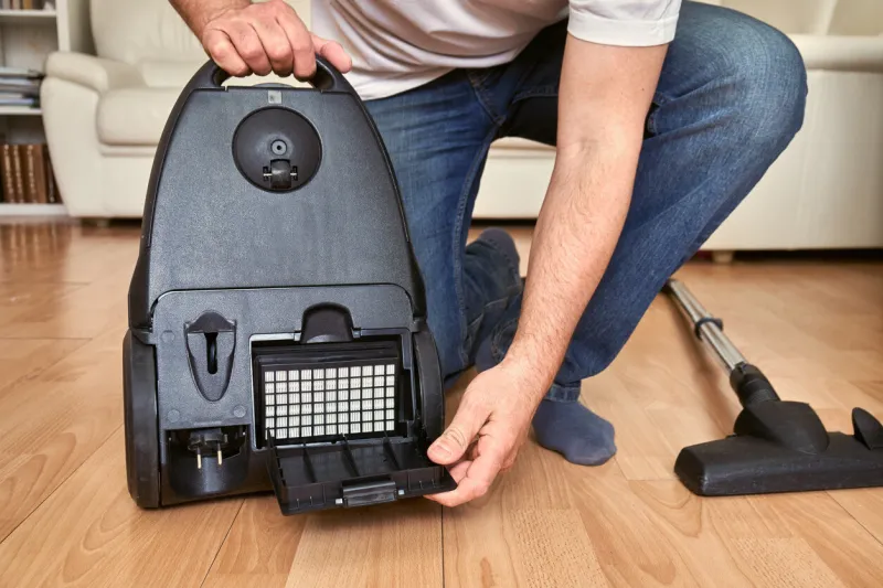 middle-aged man replacing an air filter in a vacuum cleaner at home on the floor