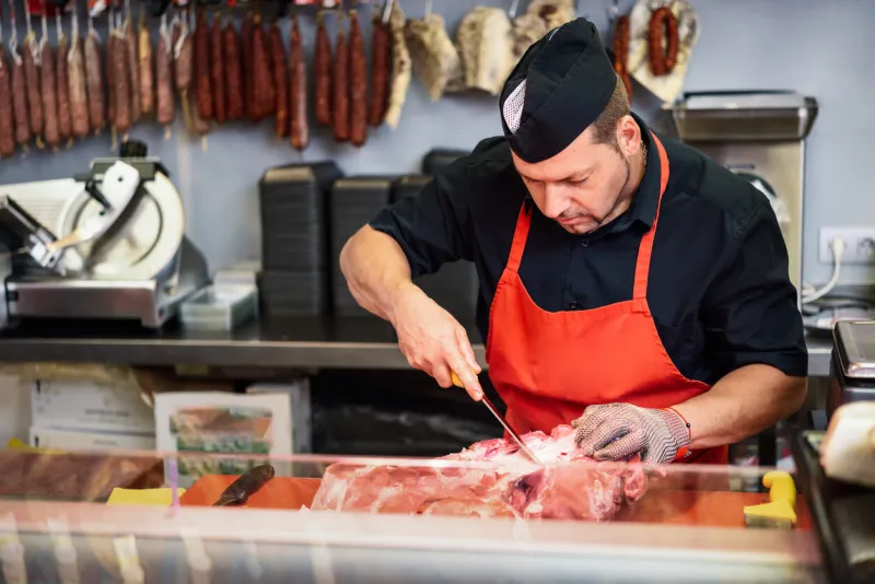 male butcher boning fresh ham in a modern butcher shop with metal safety mesh glove