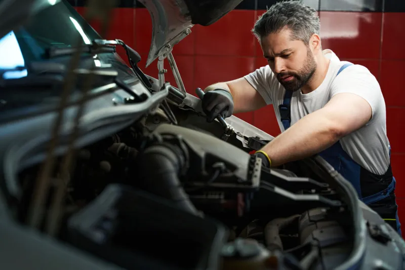 serious focused automotive service technician tightening parts on customer vehicle with wrench