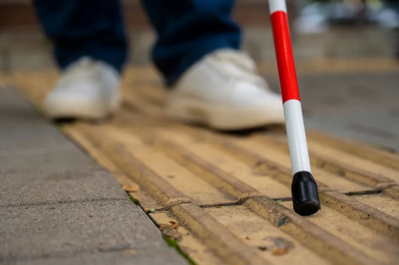 a blind woman walks on the street on tactile yellow tiles focus on the tactile cane