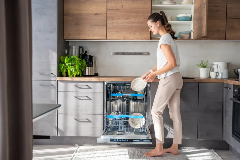 a woman removes clean ceramic dishes from the dishwasher household and useful technology concept high quality photo