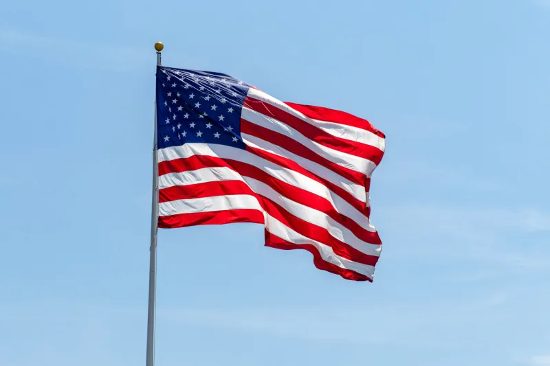 american flag waving on pole with bright vibrant red white and blue colors against blue sky