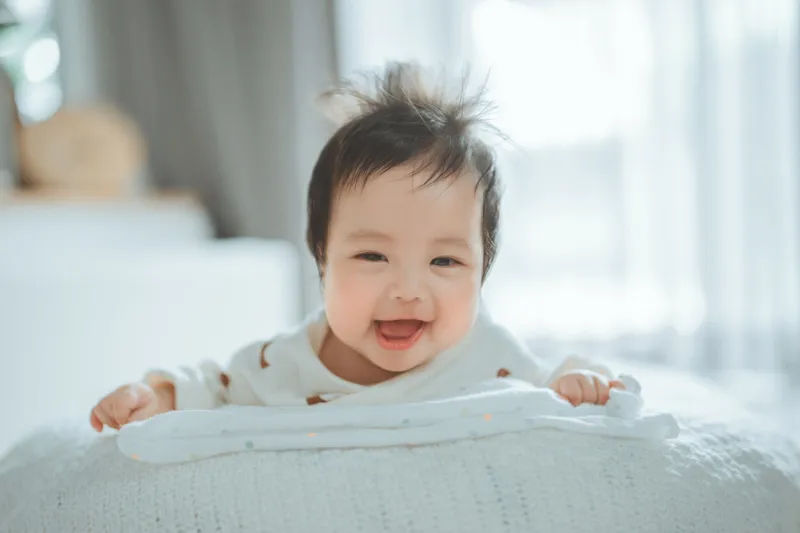 happy cheerful cute little asian 4 - 6 months old baby girl doing tummy time looking at camera, newborn baby laying on stomach developing neck control