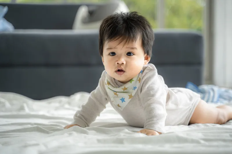 an asian baby is crawling along the floor on a room covered by a quilt