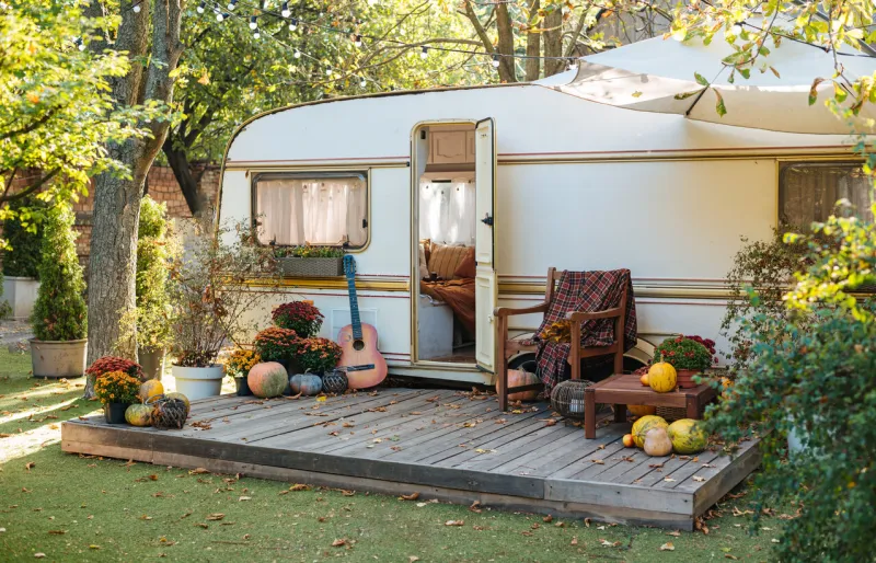 mobile home van with terrace at sunset in autumn, mobile home, orange fallen leaves autumn decor, pumpkins