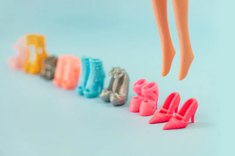 plastic doll legs in toy shoes and a lot of different stylish fashionable shoes on a pink background educational games for children changing shoes games put on shoes