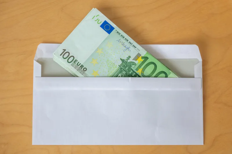 a stack of 100 euro banknotes in a white envelope on a wooden table