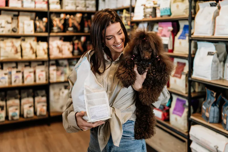 beautiful young woman enjoying in modern pet shop together with her adorable brown toy poodle