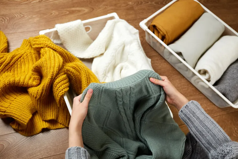 a young woman neatly puts stacks of knitted clothes into a metal laundry basket the concept of restoring order, cleaning, cluttering, organizing space