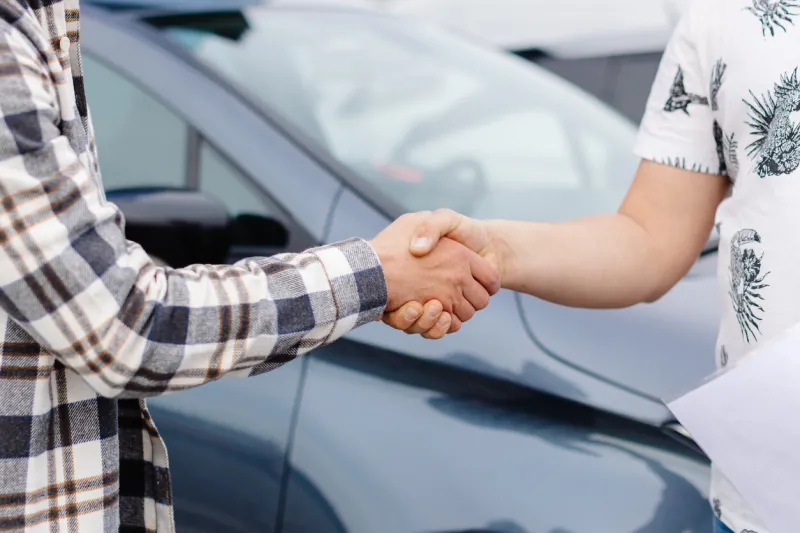 man buying car and shaking hands with salesman against blurred auto, closeup concept of choosing and buying new car at showroom