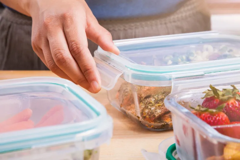 a woman meal preps in the kitchen she is putting black berries, strawberries, peas, and nuts into clear glass food storage containers with lids