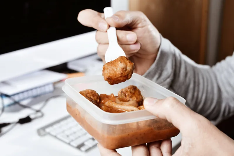 closeup of a young caucasian man eating lunch from a plastic container at the office