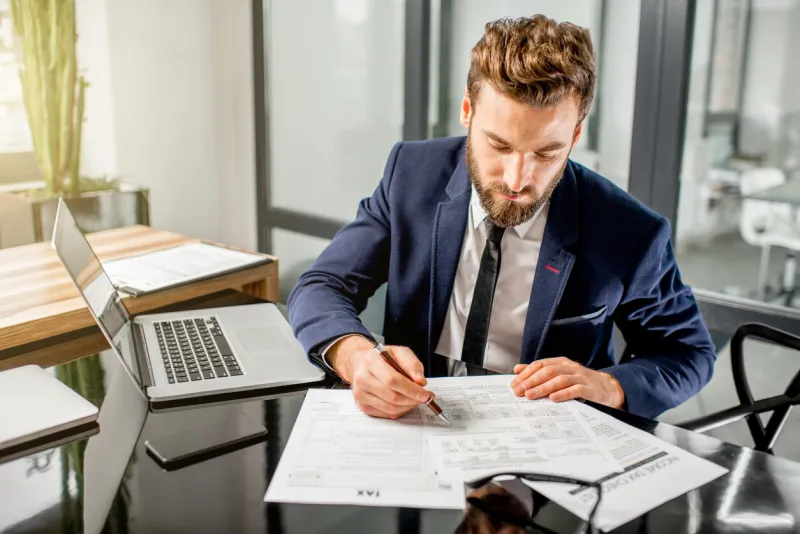 handsome tax manager dressed in the suit working with documents and laptop at the modern office interior