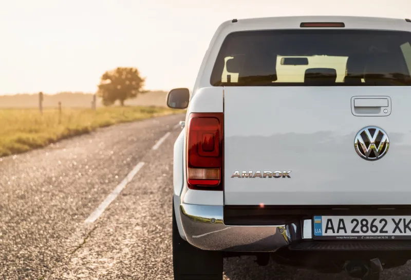 volkswagen amarok on a paved road in late afternoon rear view of vw pickup truck against the sun, lone tree on the left kyiv region, ukraine - june