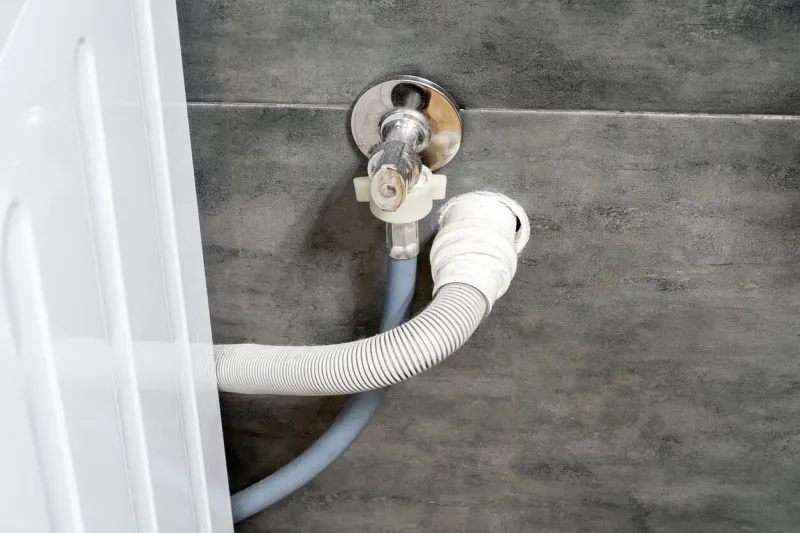dirty drain and water hoses for the washing machine running into a wall covered with gray concrete tile design options in a comfortable modern bathroom
