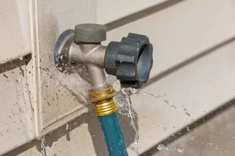 water leaking from garden hose on outdoor spigot water waste, conservation and home repair concept