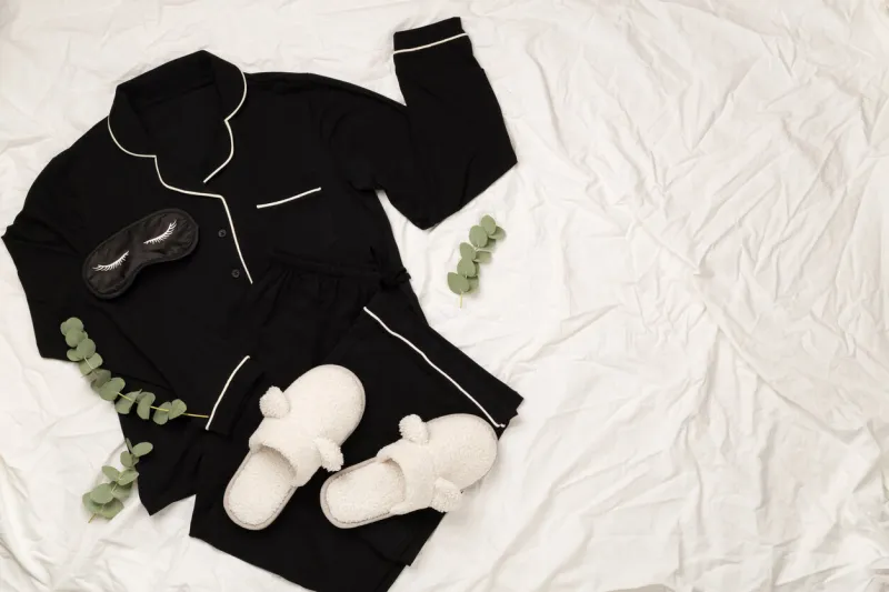 black trendy pajamas, sleeping mask and accessories on bed, top view