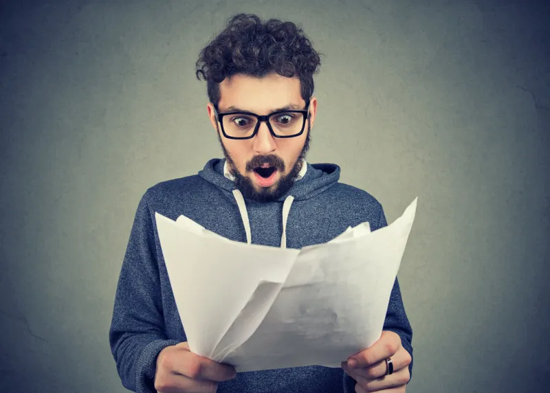 handsome man in eyeglasses exploring documents and looking shocked with results