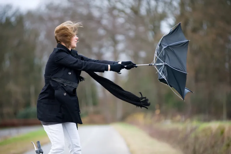 a young woman is fighting against the storm with her umbrella