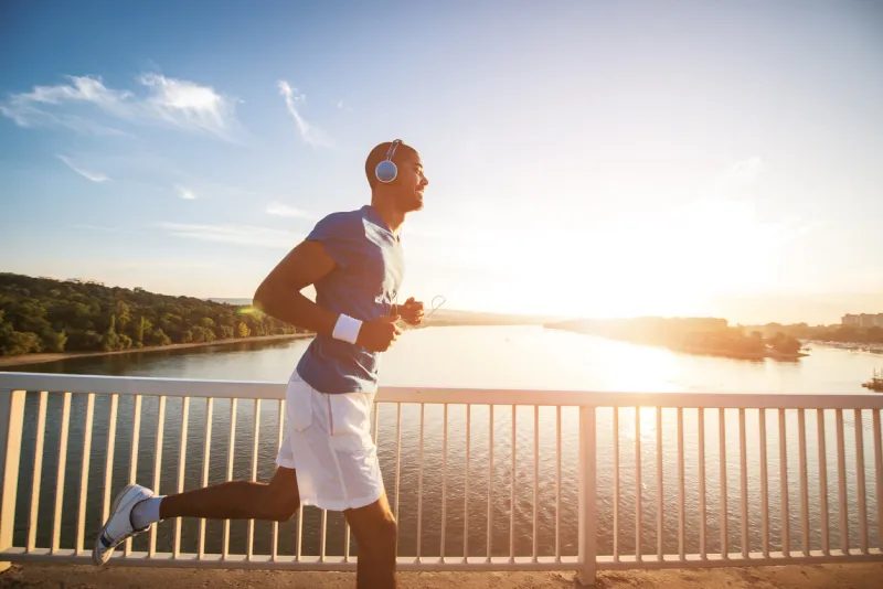 a young man running on the bridge along a river lens flare, warm tones