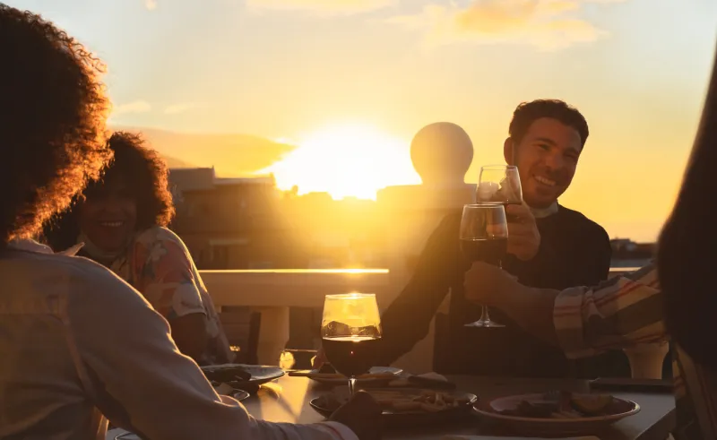 young friends toasting with red wine at appetizer sunset time on patio house - drink and food concept