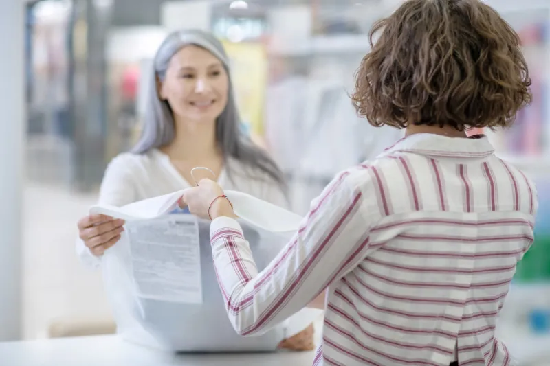 customer service woman in striped blouse behind counter with back to camera giving order to joyful long-haired customer