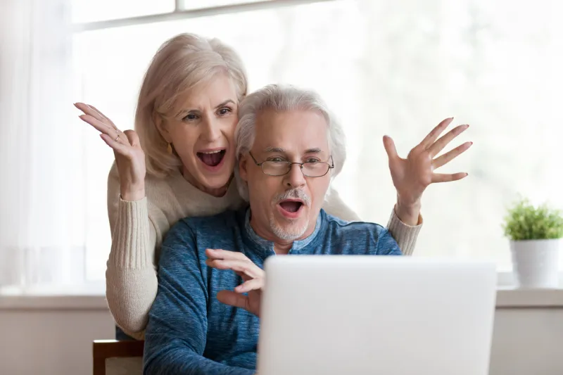 excited senior mature couple surprised by good unbelievable news, unexpected win, huge shopping sale offer on website, astonished older middle aged family looking at computer screen feeling amazed