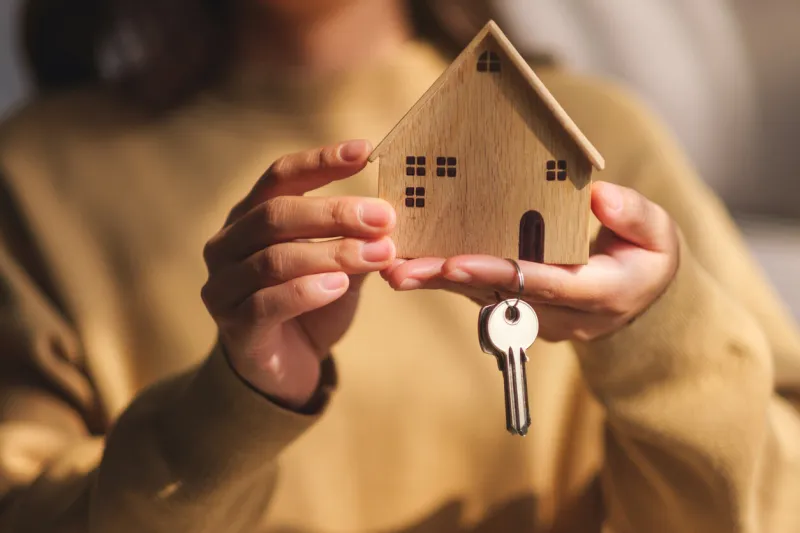 closeup image of a woman holding a wooden house model and the keys for real estate concept