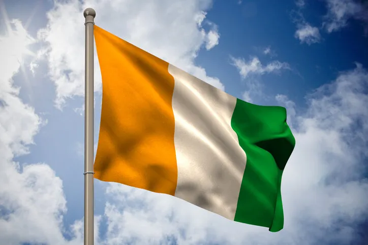ivory coast national flag on flagpole against bright blue sky with clouds