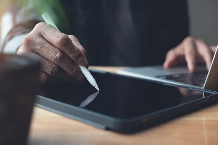 close up of man hand using stylus pen signing e-document on digital tablet and working on laptop computer at home office, e-signing, online job, telecommuting, working at home
