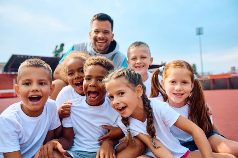 group of happy kids and their pe teacher during sports training at the stadium