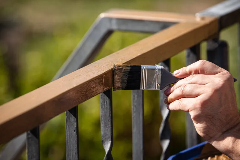 a man is painting a metal railing with copper varnish, close up outdoor shot