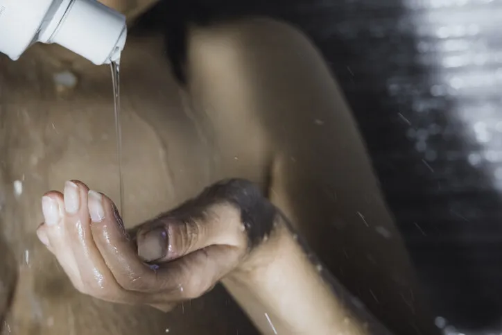 middle eastern mature adult woman putting bath gel on her hand to soap herself in the shower with hot water