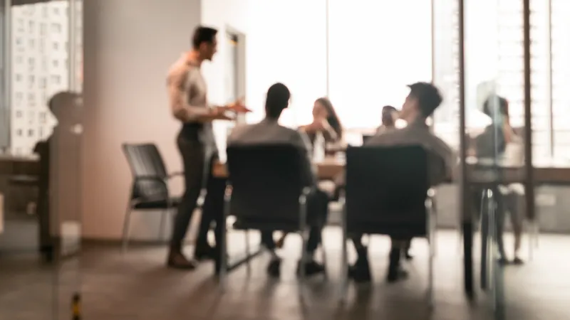 business presentation, blurred background businessman giving speech during seminar with coworkers in office, standing at desk in boardroom, diverse people sitting at table and listening to speaker