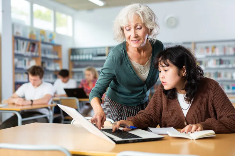 elderly female teacher helps schoolgirl solve the equation in the school library