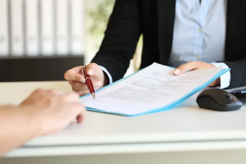 close up of an executive hands holding a pen and indicating where to sign a contract at office
