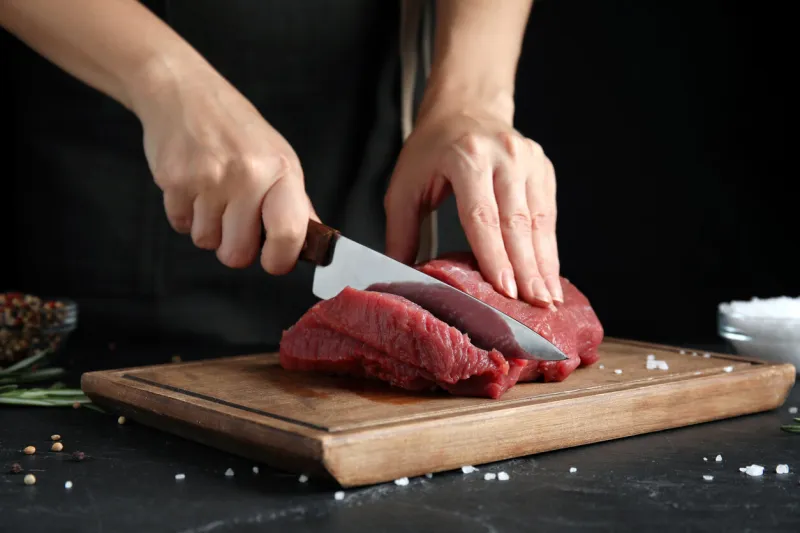 woman cutting fresh raw meat at black table, closeup