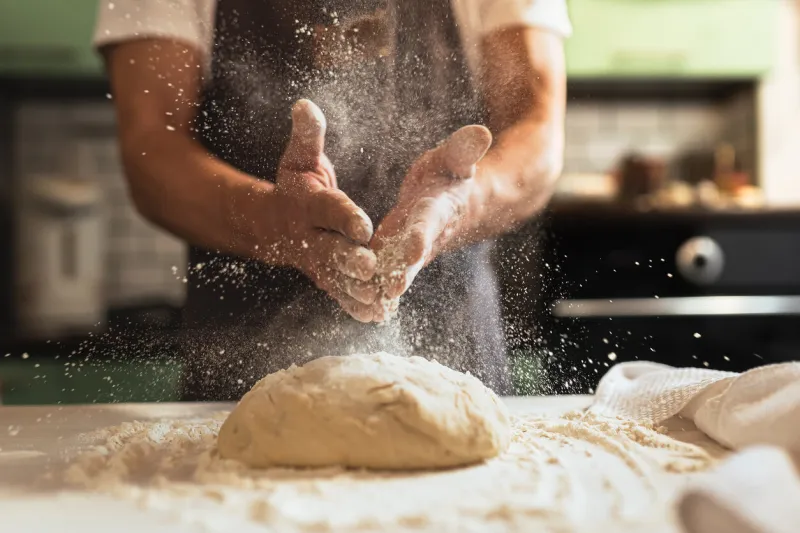 kneading dough male chef in kitchen chef's apron spraying flour over dough