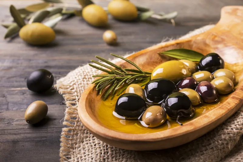 wooden bowl in the foreground with rosemary olives and virgin oil on the wooden table