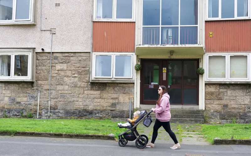 paisley, scotland, uk, august 7th 2022 mother walking past council flats in poor housing estate with many social welfare problems uk