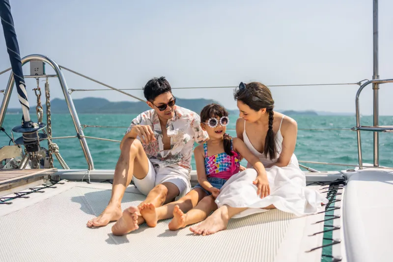 asian happy family sitting on deck of yacht while yachting outdoor young beautiful couple hanging out and spend time with daughter while catamaran boat sailing during holiday summer trip together