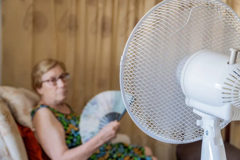 electric fan cooling an elderly woman sitting on the sofa in the living room