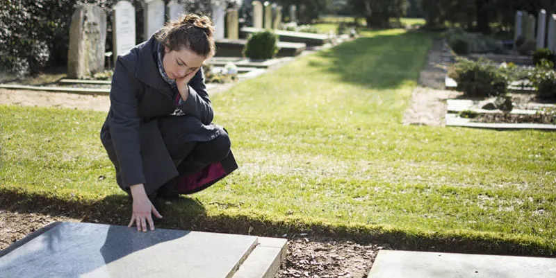 woman sitting at grave with hand on grave