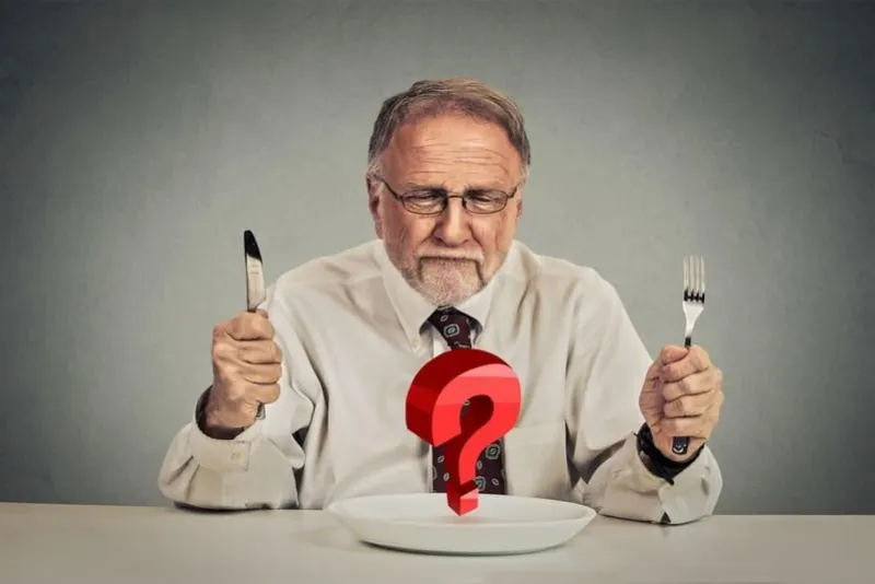 elderly man with silverware looking at plate with question mark having problems with diet