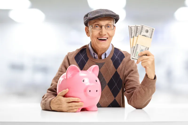 senior with a piggybank and bundles of money seated at a table