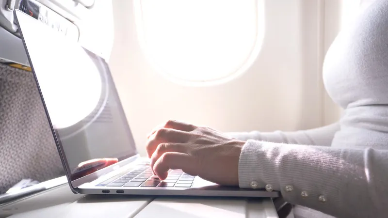 close up  unrecognizable woman types on her modern laptop while flying overseas in first class young female traveler writing a blog post of her recent summer vacation during her long flight back home