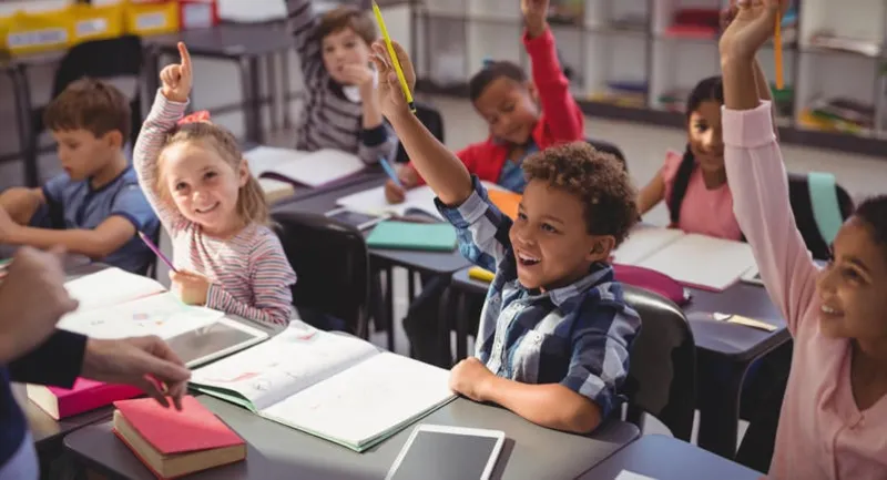schoolkids raising their hands in classroom at school