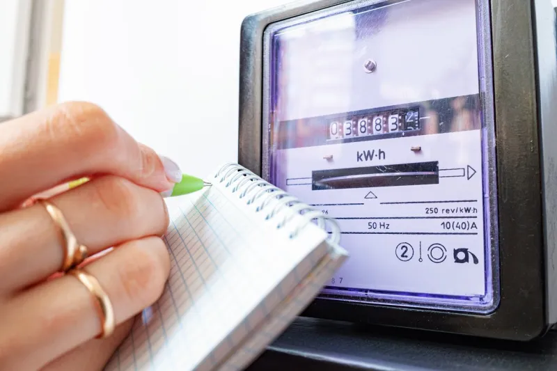 woman's hands with pen and notepad writes the electricity meter readings at home